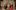 A group of actors, on stage, in Russian costumes, in the process of lining up to have their photo taken. They are smiling and laughing.