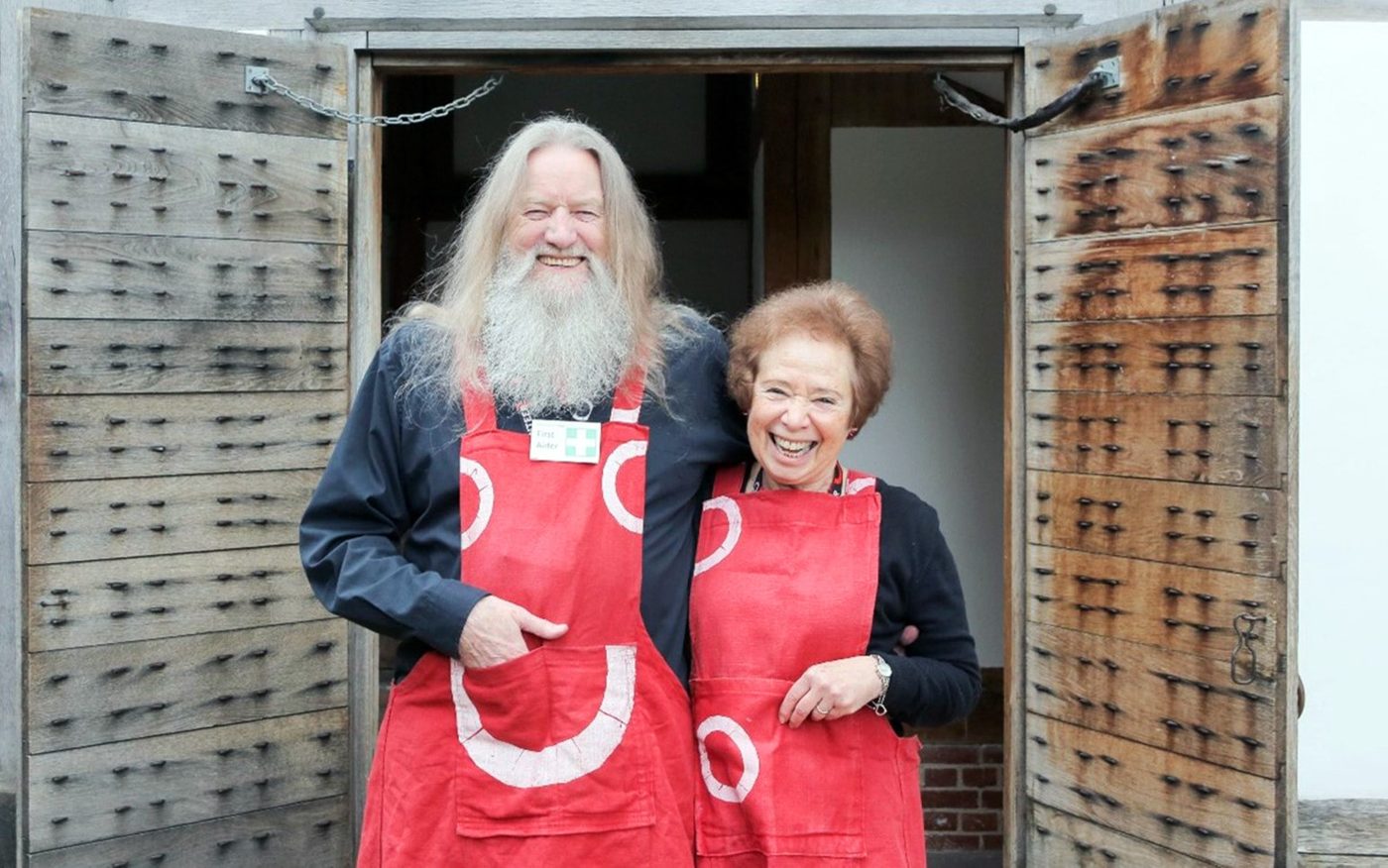 Access Ambassador Volunteer Shakespeare’s Globe - Terry, Cathie (2) Two Globe Volunteers standing outside the East Tower entrance, wearing red Globe-brand aprons.